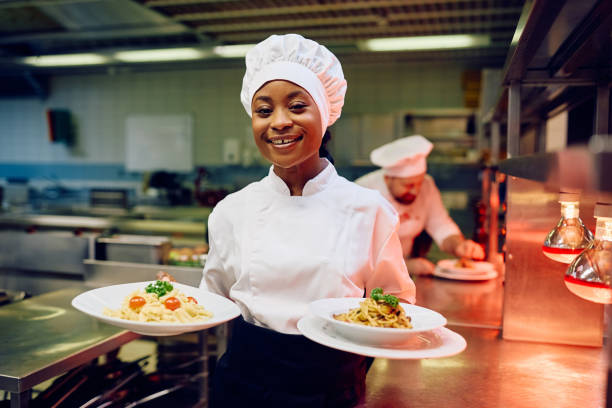 daea Happy African American female chef serving a dish in restaurant and looking at camera.